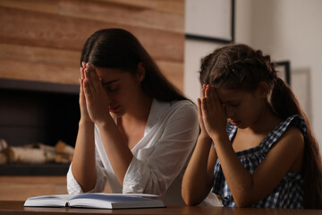 Young woman with her little daughter praying together over Bible at home
