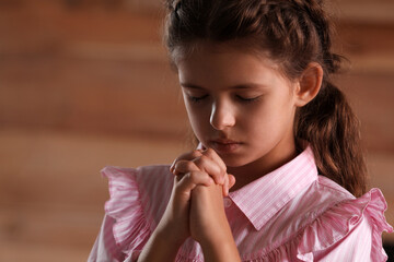 Cute little girl with hands clasped together praying on blurred background