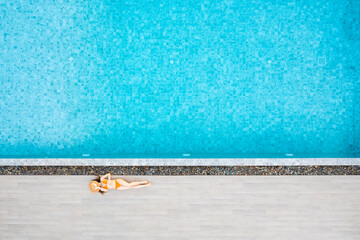 Top view of slim young woman in hat relaxing in resort swimming pool. Female enjoying sunbathing.