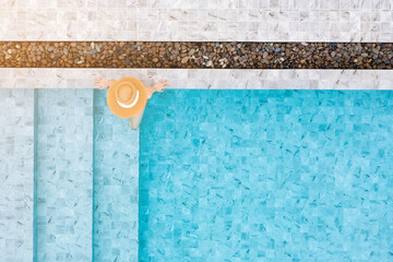 Top view of slim young woman in hat relaxing in resort swimming pool. Female enjoying sunbathing.