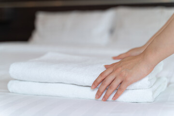 Obraz na płótnie Canvas Closeup hands putting a stack of new clean bath towels on the bed. Hotel room service concept.