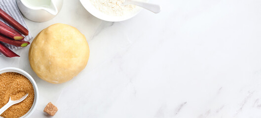 Ball of dough and ingredients flour, water, butter, sugar and rhubarb for baking on white marble background with dusting of flour. Recipe step by step. Selective focus. Top view. Banner.