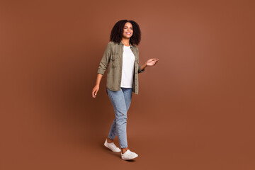 Fototapeta na wymiar Full size photo of nice young brunette lady go wear shirt jeans shoes isolated on brown color background
