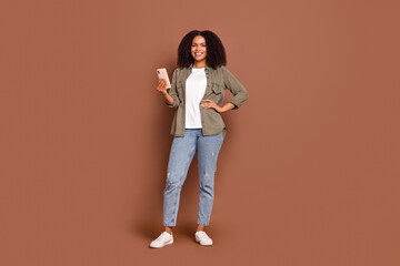 Full body photo of nice young brunette lady look telephone wear shirt jeans shoes isolated on brown background