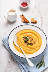 Pumpkin traditional soup with creamy silky texture with sage leaves and red pepper in white plate or bowl. Light grey background. Copy space. Mock up. Top view, flat lay.