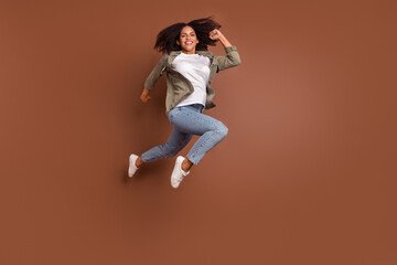 Fototapeta na wymiar Full size photo of hooray millennial brunette lady jump wear shirt jeans shoes isolated on brown background