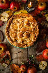 Autumn fruit pie decorated with crust apple pattern, apples,  lingonberries, candle and fallen leaves on old wooden table. 