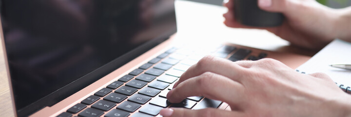 Female hands typing on laptop keyboard holds glass with coffee