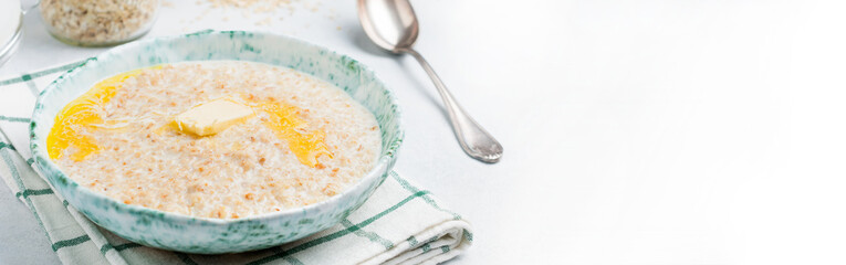 Oatmeal with butter in a ceramic plate on a light stone or concrete background. Selective focus