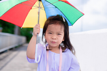 Kindergarten students walk with colorful umbrellas to protect her skin from direct afternoon sunlight. A cute girl is walking home. Child wear white shirt.