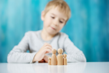 Child with wooden figures of the family on the blue background - obrazy, fototapety, plakaty