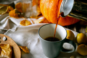 There is a layout of pumpkin and autumn leaves on the kitchen table with cappuccino 