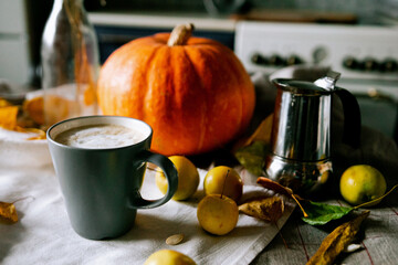 There is a layout of pumpkin and autumn leaves on the kitchen table with cappuccino 