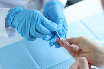 Doctor wearing disposable gloves takes blood from patient finger - obrazy, fototapety, plakaty