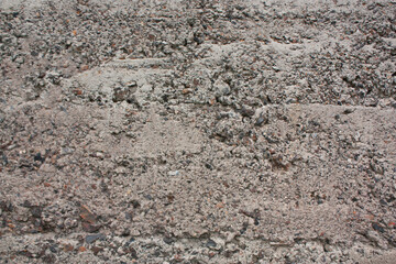 The old cinder-concrete wall is gray with damage and stones. Gray background with texture.