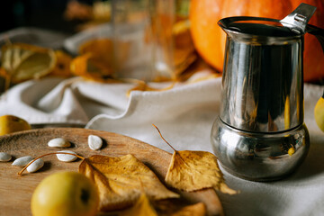 There is a layout of pumpkin and autumn leaves on the kitchen table with cappuccino 