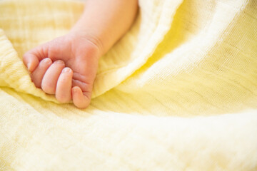 Newborn baby hand. Close up little fist over yellow muslin blanket. With copy space. Happy family concept, daycare nursery. Children's day - obrazy, fototapety, plakaty