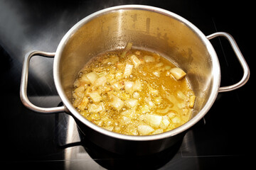 Onions are sauteed in golden brown butter in a stainless steel pot on a black induction stove, base...