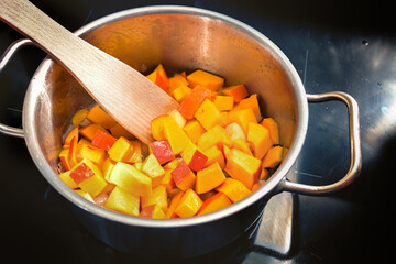 Sliced red kuri squash or Hokkaido pumpkin in a stainless steel pot on a black induction stove,...