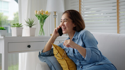 Asia elder lady people, latin mom sitting at home cozy sofa couch use digital 5G cellular cellphone on wifi wireless service support in remotely social distance call to advice, gossip, order online.