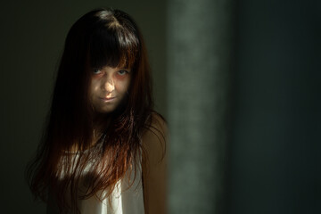 Fototapeta premium Female ghost in white dress in room. A young scary girl in an old white dress staring in to the camera ferociously with dark background. Asian woman make up ghost face at house. Scary horror concept.