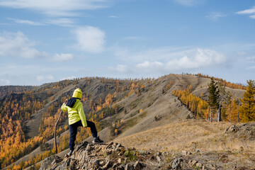 A guy in bright sportswear walks along the top of the mountain, looks forward at the mountains and forest, clear sky overhead, autumn landscape