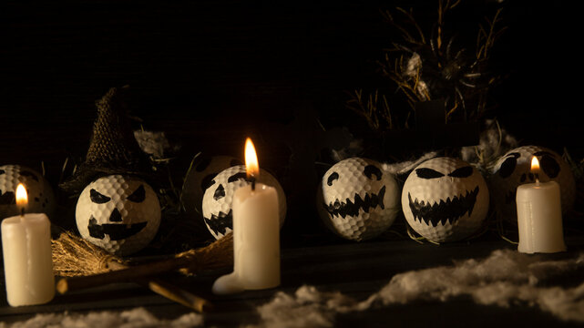 HALLOWEEN, GOLF BALLS DECORATED LIKE PUMPKINS WITH TERRORIFIC FACES WITH CANDLES, FOLIAGE, CROSSES, INSECTS ON RUSTIC WOODEN TABLE AND DARK BACKGROUND WITH SPACE FOR TEXT