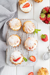 Delicious homemade small cakes profiterole choux pastry with custard, strawberry and icing powder on the white wooden background. Copy space.