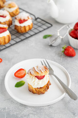 Delicious homemade small cakes profiterole choux pastry with custard, strawberry and icing powder on a gray concrete background. Copy space.
