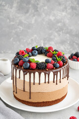 Three chocolate mousse cake with chocolate glaze, blueberries, raspberries and blackberries on top on a white plate on a dark wooden background. Cake with three layers of different taste. Copy space.