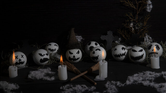 HALLOWEEN, GOLF BALLS DECORATED LIKE PUMPKINS WITH TERRORIFIC FACES WITH CANDLES, FOLIAGE, CROSSES, INSECTS ON RUSTIC WOODEN TABLE AND DARK BACKGROUND WITH SPACE FOR TEXT