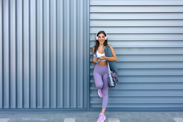 Obraz premium Image of a beautiful strong happy cheerful young sports woman posing texting with bottle of water .Happy young woman in sports clothing smiling. Muscular fitness model