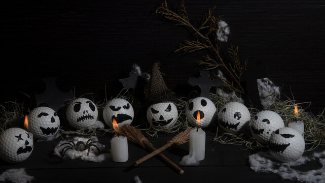 HALLOWEEN, GOLF BALLS DECORATED LIKE PUMPKINS WITH TERRORIFIC FACES WITH CANDLES, FOLIAGE, CROSSES, INSECTS ON RUSTIC WOODEN TABLE AND DARK BACKGROUND WITH SPACE FOR TEXT