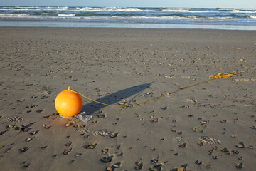 Shiny orange plastic float with yellow rope washed ashore at Skagen Nordstrand near Cape Grenen, meeting point of Skagerrak and Kattegat and the northernmost point of Denmark, Skagen, Northern Jutland