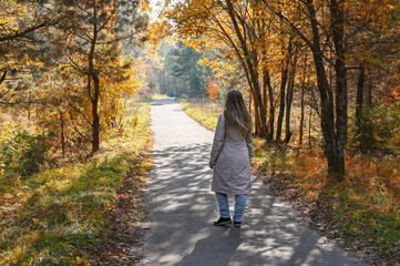 A young woman walking in the autumn park. Hello october. Beautiful trees with dried colourful leaves