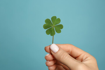 Woman holding green four leaf clover on light blue background, closeup - Powered by Adobe