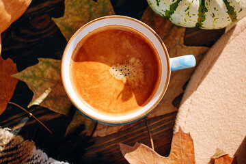 autumn still life with a cup of coffee. autumn leaves, pumpkins, a plaid and a hat on a wooden table and a cup of hot aromatic coffee in the center.