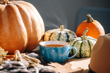 autumn still life with a cup of coffee. autumn leaves, pumpkins, a plaid and a hat on a wooden table and a cup of hot aromatic coffee in the center.