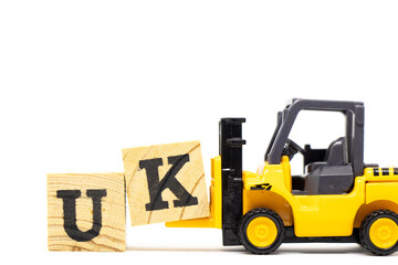 Toy forklift hold letter block k to complete word UK  (abbreviation of united kingdom) on wood background