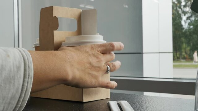 the hands of a Caucasian woman place a cardboard stand with two bio paper cups with cappuccino on the table. biodegradable disposable tableware. environmental concern