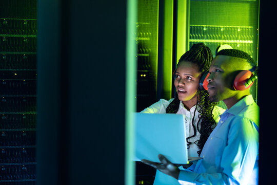 African american computer technicians wearing headphones using laptop working in server room