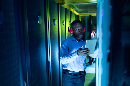 African american male computer technician wearing headphones using tablet working in server room