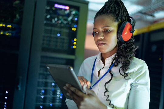 African american female computer technician wearing headphones using tablet working in server room