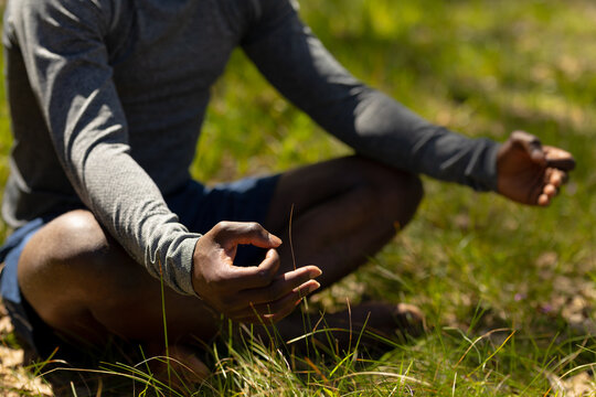 Relaxing african american man sitting with crossed legs and meditating in countryside
