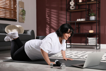 Fototapeta na wymiar Overweight mature woman doing exercise while watching online class at home