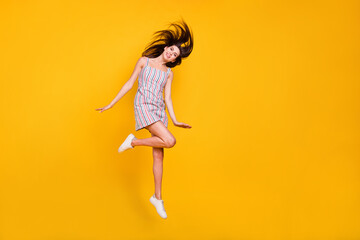 Fototapeta na wymiar Full length body size woman smiling jumping high happy throwing hair isolated vivid yellow color background