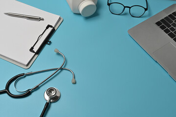 Top view with a stethoscope, pill bottle, eyeglasses, pen, laptop and blank paper on the clipboard. Top view with copy space, flat lay.