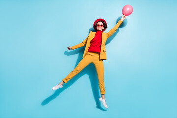 Fototapeta na wymiar Photo of cool pretty young lady wear yellow blazer red cap smiling jumping flying balloon isolated blue color background