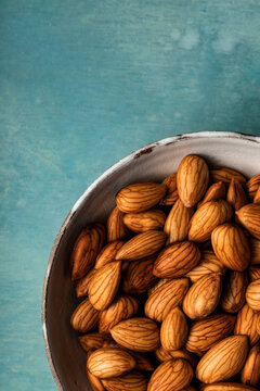 A closeup overhead view of a bowl of almonds shot on a blue background