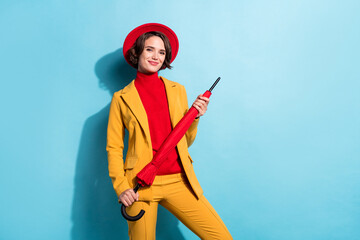 Photo of charming pretty young woman dressed red headwear holding umbrella empty space smiling isolated blue color background © deagreez